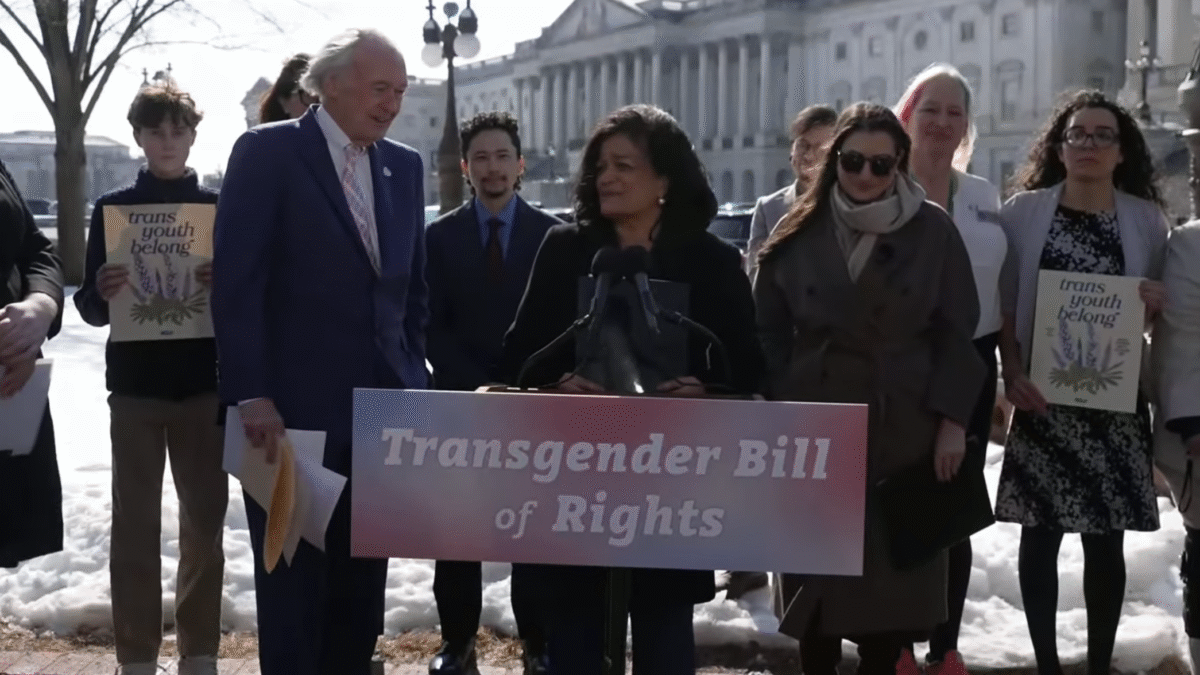 Trans rights activists join members of Congress behind a pink sign that says 