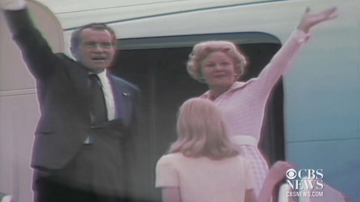 In a dark suit, Richard Nixon waves goodbye from the door of Air Force One, with Patricia Nixon at his side.