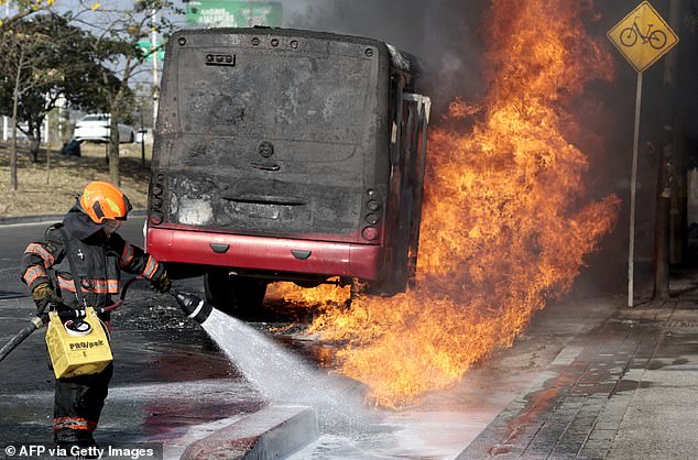 A firefighter extinguishes a burning bus set on fire by organised crime groups in response to an operation in Jalisco to arrest a high-priority security target, at one of the main avenues in Zapopan, state of Jalisco, Mexico, on February 22, 2026. Armed civilians blocked several roads in the state of Jalisco, in western Mexico, following an operation by federal forces in the town of Tapalpa, local authorities reported. Jalisco, which will host four matches of the upcoming 2026 World Cup, is home to the powerful Jalisco New Generation Cartel (CJNG), and has been rocked by several episodes of violence in recent years. (Photo by Ulises Ruiz / AFP via Getty Images)
