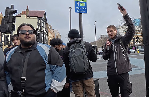 A male clutching a microphone and Bible (right) can be heard preaching the Gospel in Whitechapel Road, just yards from the East London Mosque