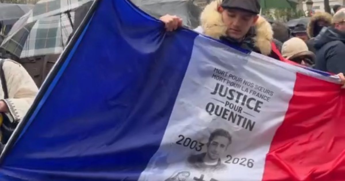Protestor holding a French flag with a tribute to Quentin, featuring a photo and the text "Justice pour Quentin," during a demonstration in Paris.