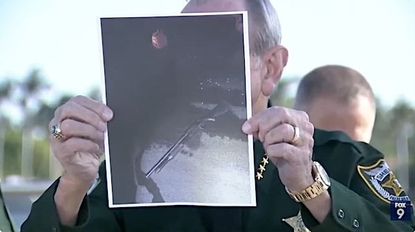 Palm Beach County Sheriff Ric Bradshaw holds a photo of the shotgun carried by a man scaling the north gate at President Donald Trump's Mar-a-Lago home on Sunday, Feb. 22, 2026