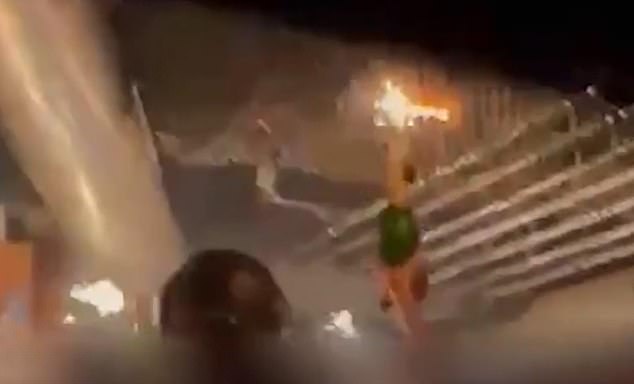 Partygoers can be seen dancing and cheering as a waitress wearing a helmet is carried on a man's shoulders through the club, holding champagne topped with lit sparklers