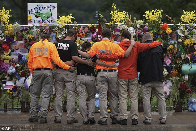 Members of a search and rescue team embrace as they visit a memorial wall for flood victims