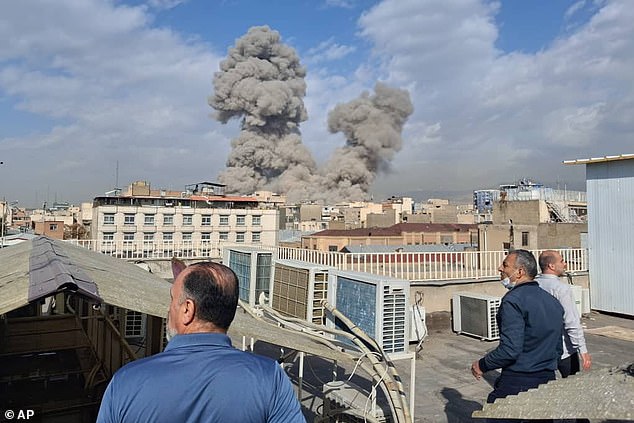 People watch as smoke rises on the skyline after an explosion in Tehran, Iran