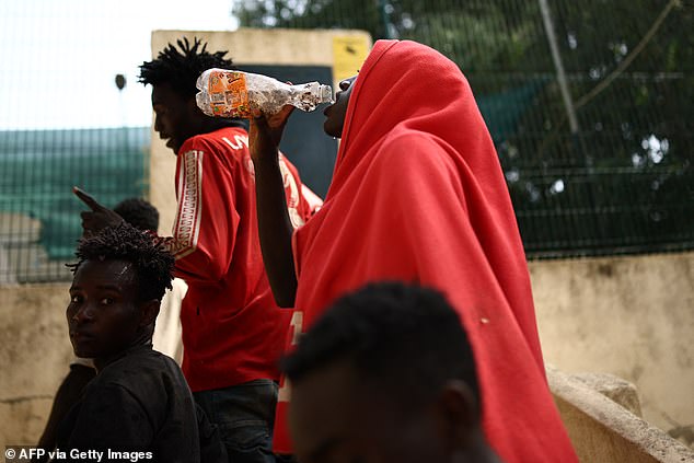 A woman drinks water outside the CETI short-stay migrant centre in Ceuta on August 1