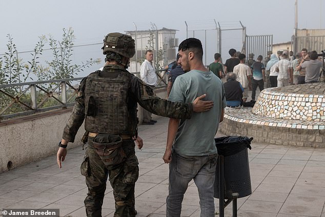 A Spanish soldier escorts a migrant away from the area as the unprecedented humanitarian response ensues