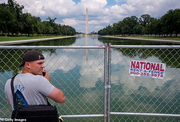 The Washington Monument is visible as a visitor takes a picture of the Reflecting Pool though a chain link fence on the National Mall