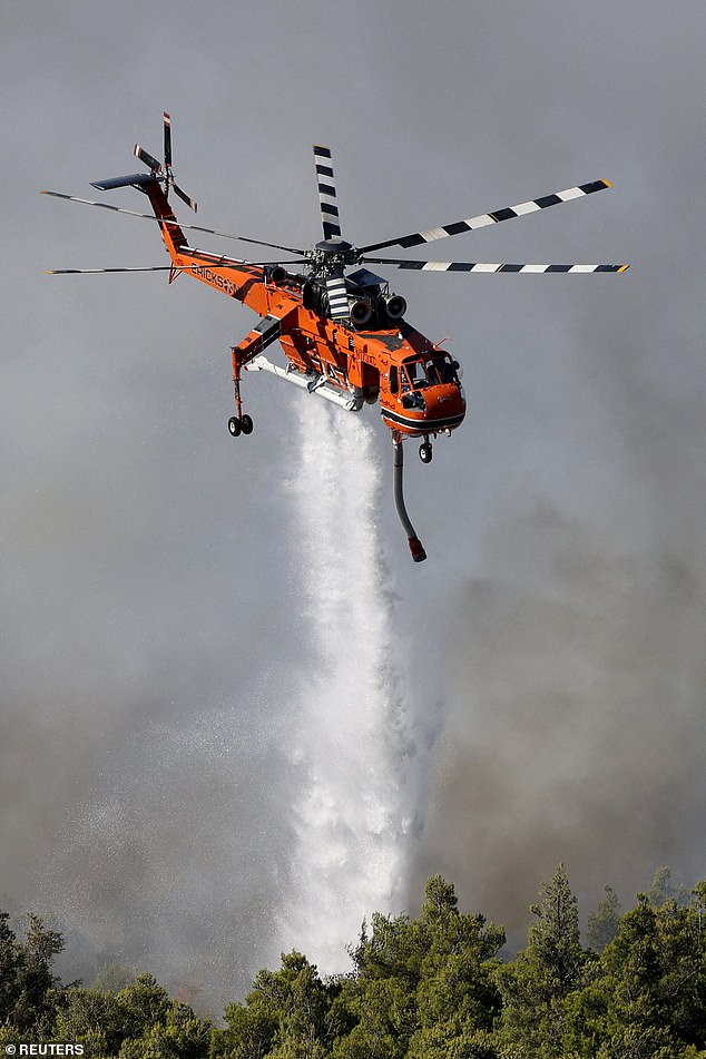 A helicopter drops water as a wildfire burns near the village Agios Nektarios, Greece