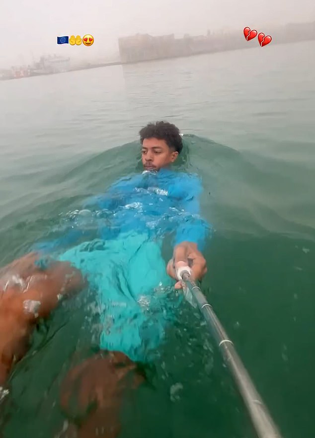 A migrant films himself swimming with a selfie stick as music plays in the background