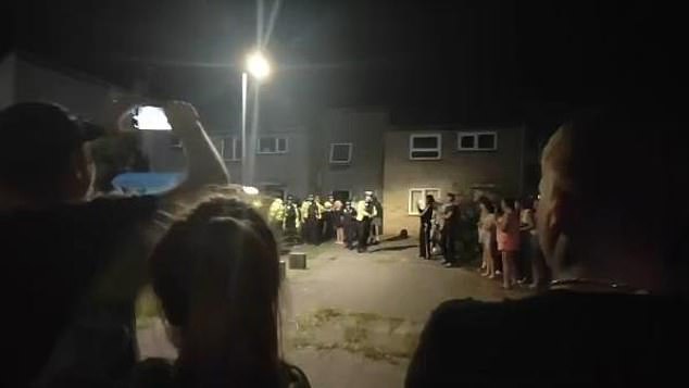 Police guard a property in the market town as protesters stand outside