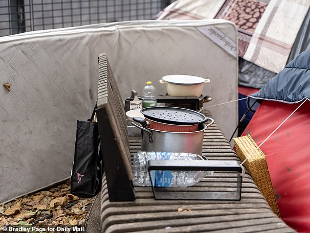 A makeshift kitchen station stores the group's utensils while bins spill over with Pot Noodles, cans of Stella Artois beer and used tissues