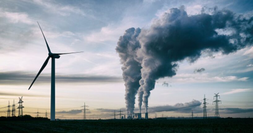 Plumes of smoke blow from a factory near a wind turbine.