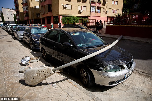 A fallen street lamp lies across a car parked on a street in a Granada suburb