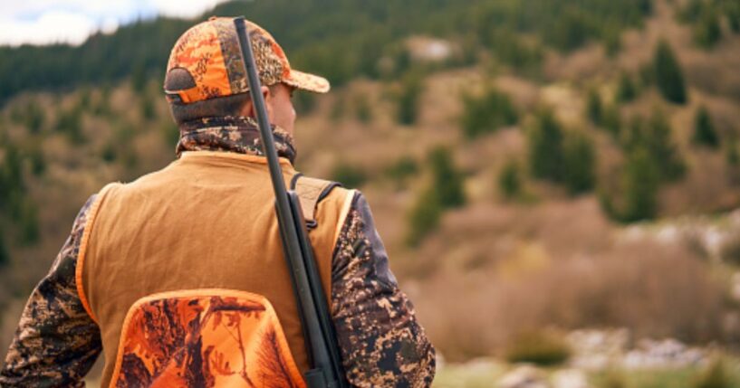 A hunter looks out at an empty field in a remote forest.