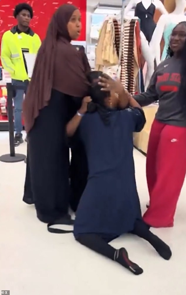 The asset protection associate, wearing a high-visibility green jacket (pictured left), stood by watching as the women, one in a navy-blue dress and the other in a black gown, rolled around striking one another in the face.