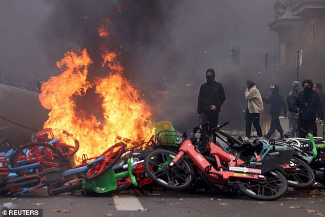 Masked protesters stand next to burning bicycles amid clashes during a demonstration against the cost of living and rising fuel prices near the Place de la Republique in Paris, October 17