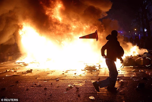Across the weekend, Demonstrations will be held across the country, with attacks likely on public buildings and state symbols as well as 'opportunistic lootings' (Pictured: a man throws a plastic traffic cone through a burning barricade amid clashes)