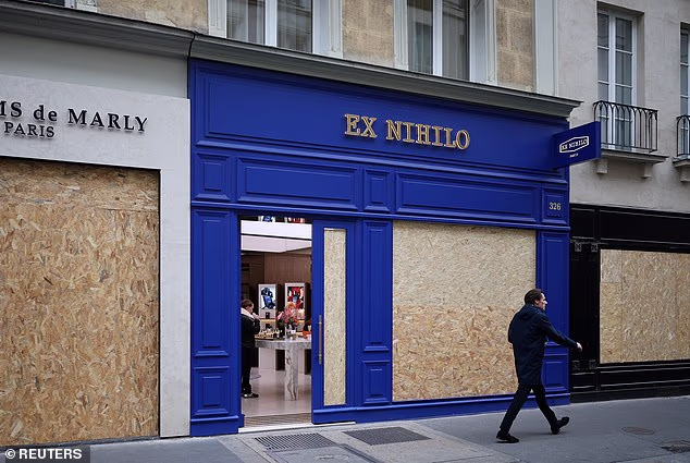A man walks past stores with display windows protected by wooden panels ahead of protests this weekend.