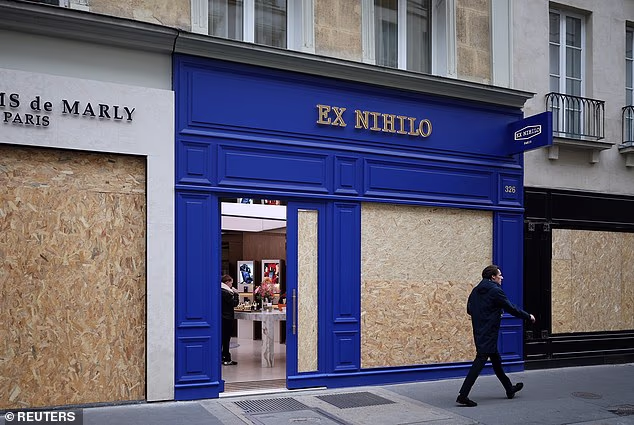 A man walks past stores with display windows protected by wooden panels ahead of protests this weekend.