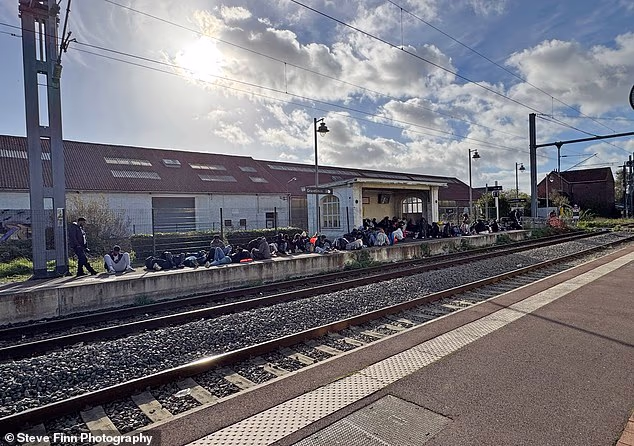 Groups of migrants sit at Gravelines train station in northern France. Daily Mail journalist Sue Reid witnessed thousands of youngsters waiting in France to set out on the traffickers' boats, either alone or with their families, in a new migrant crisis for ever-welcoming Britain