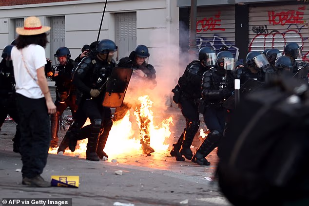 A French Gendarme who is partly burning runs in a street as facing protesters at the end of a protest march