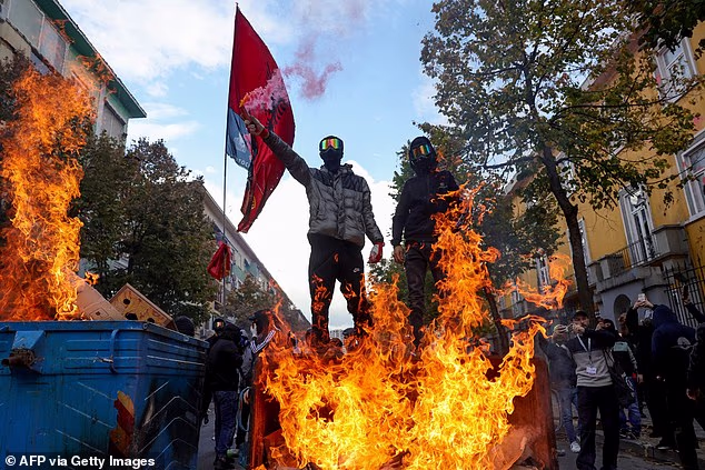 Protesters stand next to waste bins on fire during an anti-government demonstration in central Tirana, Albania